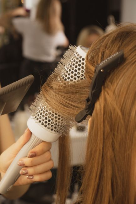 Detailed view of hairstylist curling hair in salon using a round brush and hairdryer.